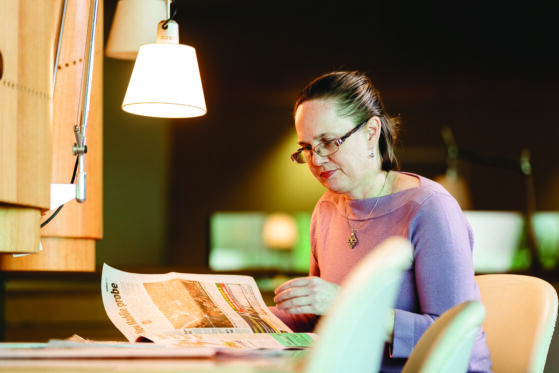 A woman reading a newspaper in a library.