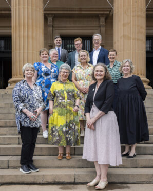 Board members and executive posing for a photograph on the stairs approaching a sandstone building.