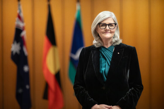 Her Excellency the Governor-General standing in front of the Australian flag, the Aboriginal flag, and the Torres Strait Islander flag.